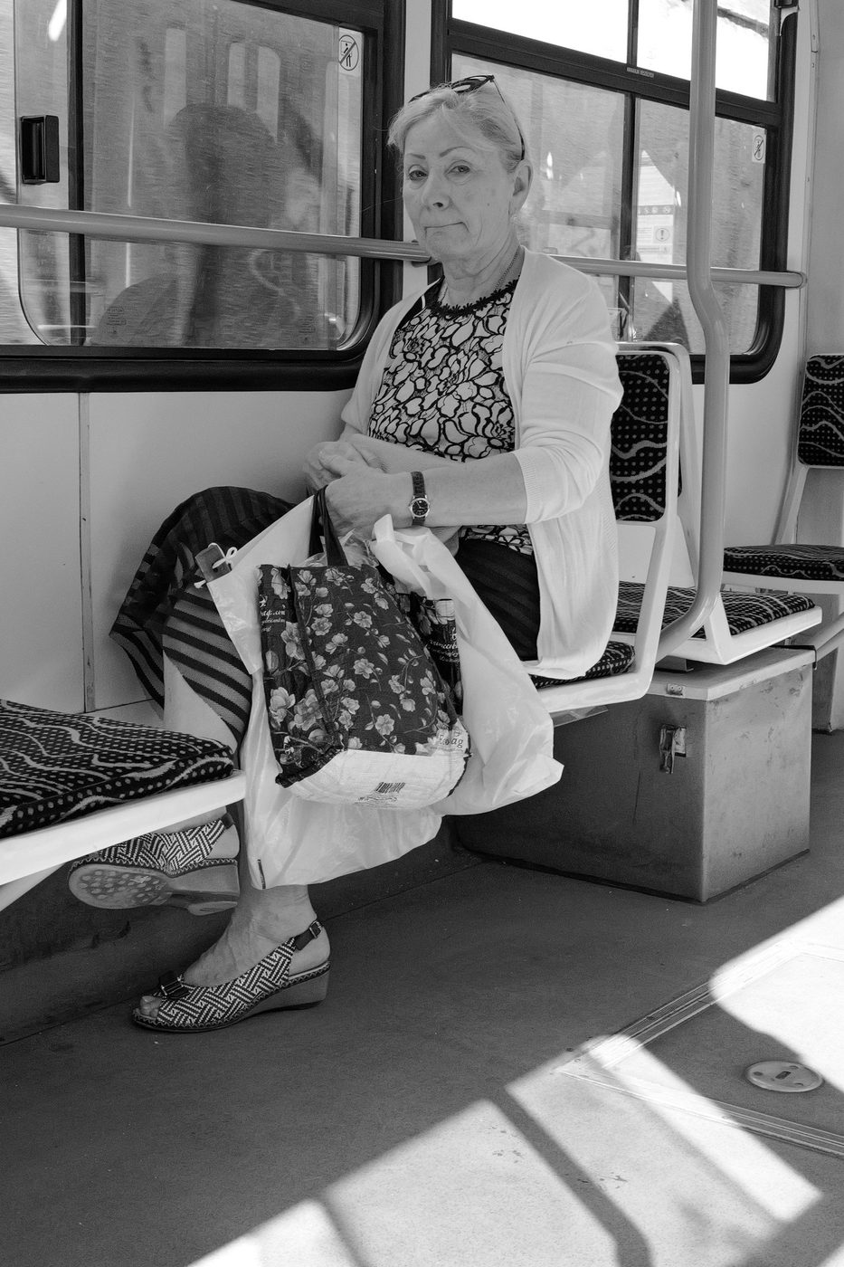 An elderly woman sitting with her shopping bags on a tram, Budapest