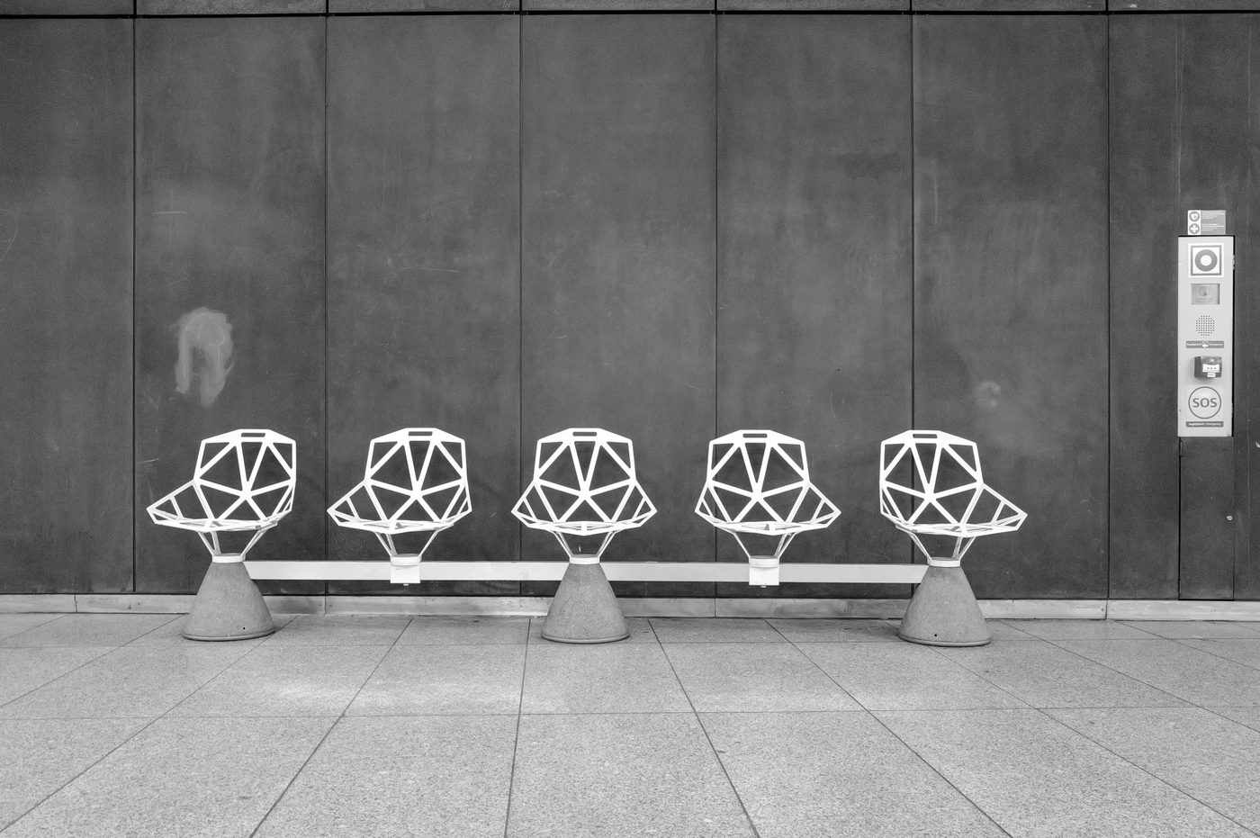 Five white perforated chairs lined up against a dark wall, metro station, Budapest