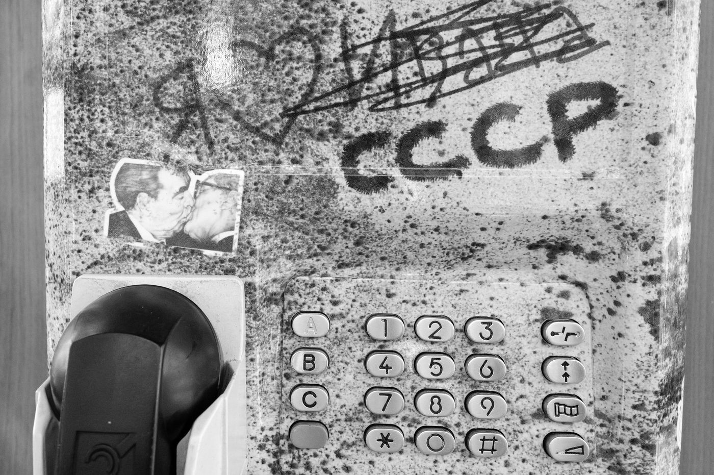 Graffiti-covered phone booth with a sticker of a kiss between leaders, Budapest