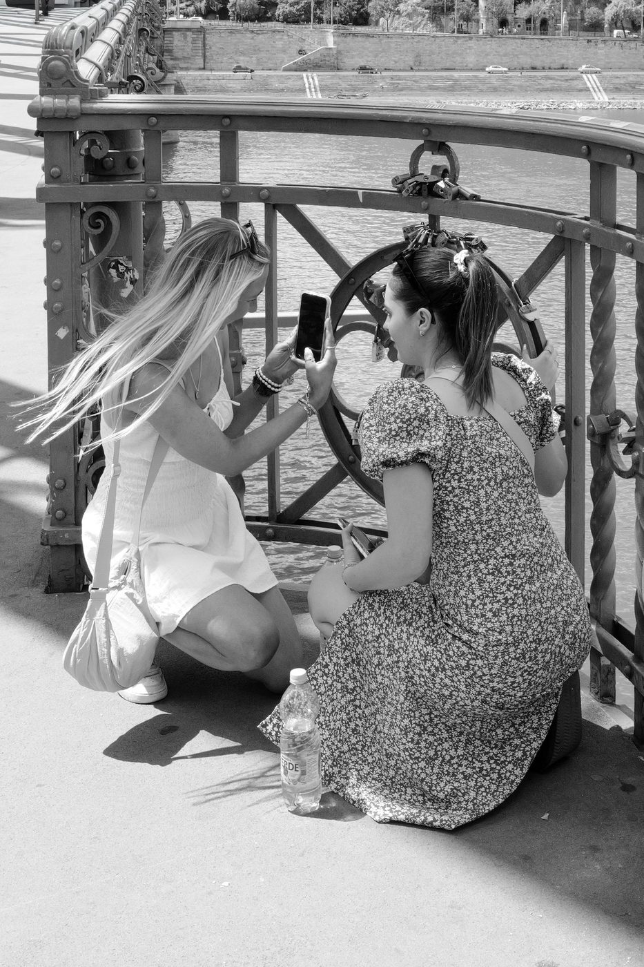 Two friends crouching near love locks on a bridge railing, Budapest