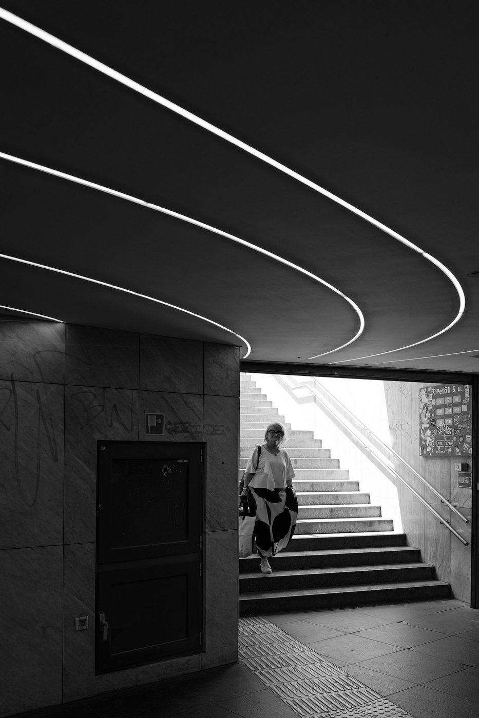 An elderly passenger going down a staircase under curved light bands, Budapest