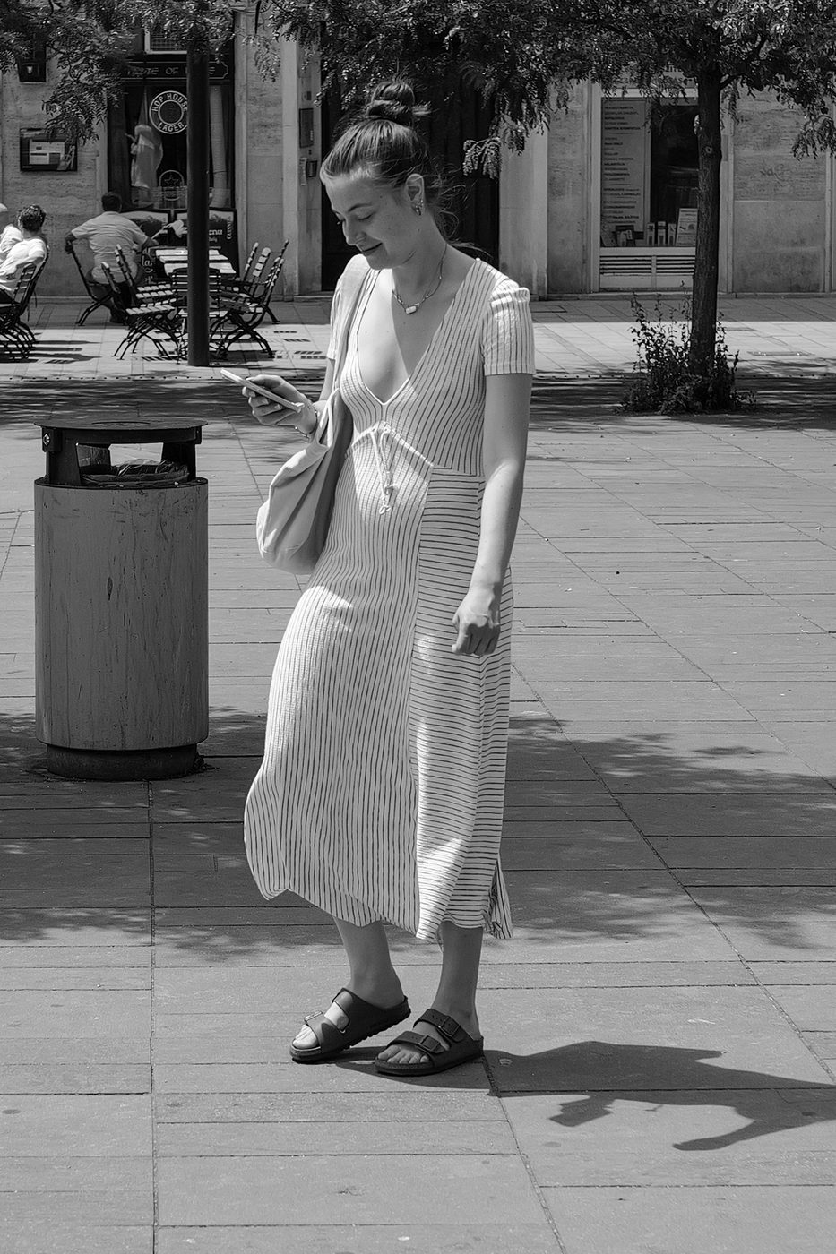 A woman in a striped dress checking her phone under the trees, Budapest