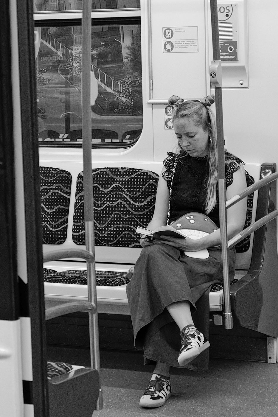 A passenger with blonde hair buns reading a book on the tram, Budapest