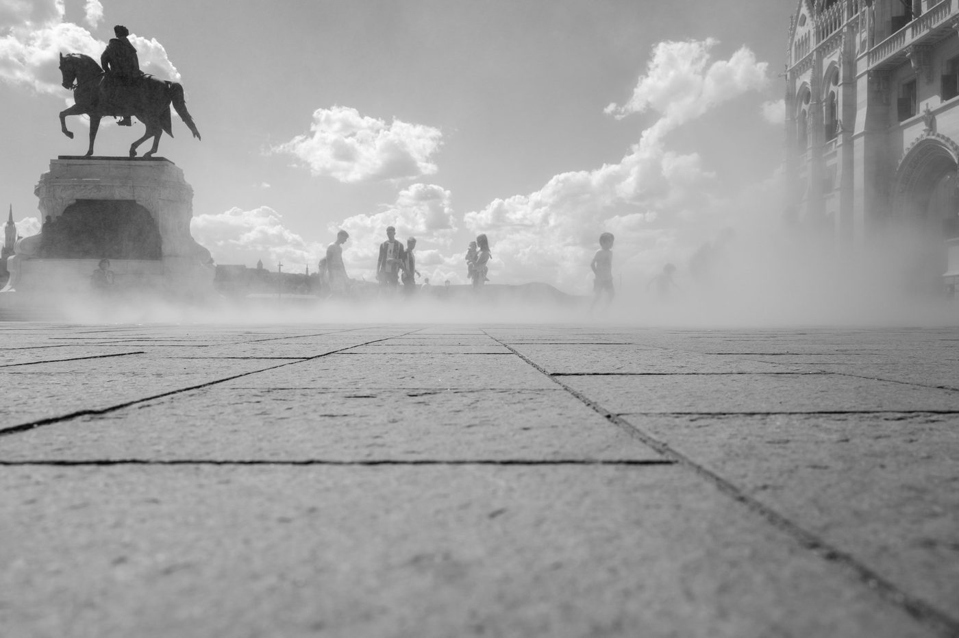 Equestrian statue in the mist of a fountain, silhouettes of passers-by, Budapest