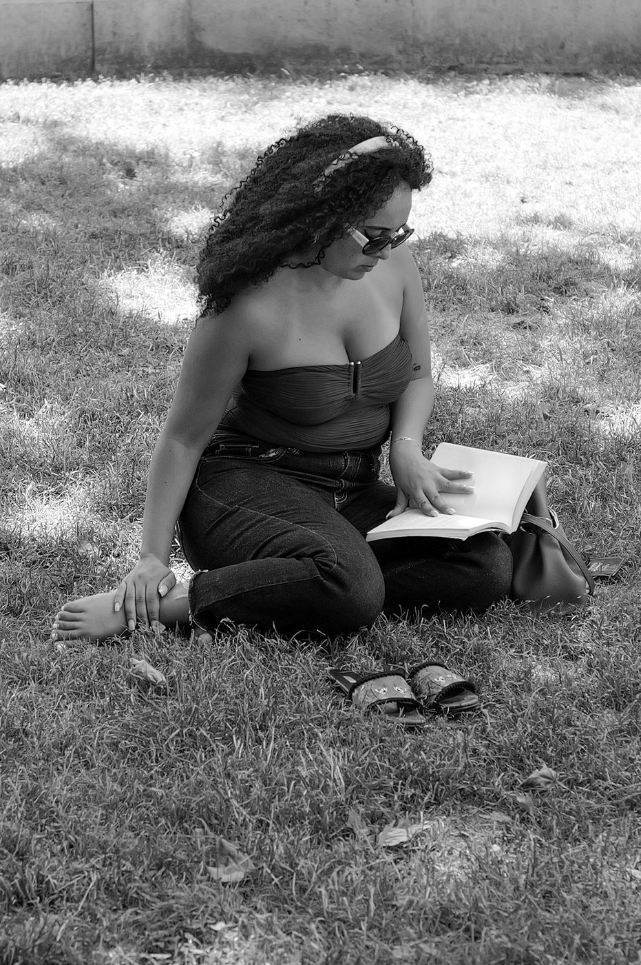A woman with curly hair reading, sitting cross-legged on the lawn, Budapest