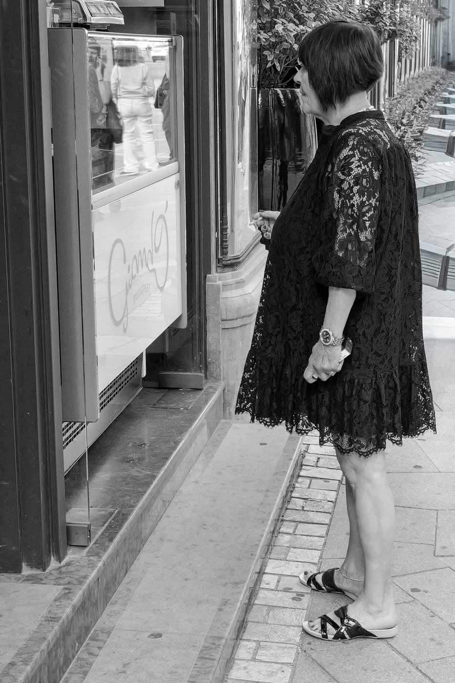 A woman in a black lace dress looking at a jewelry shop window, Budapest