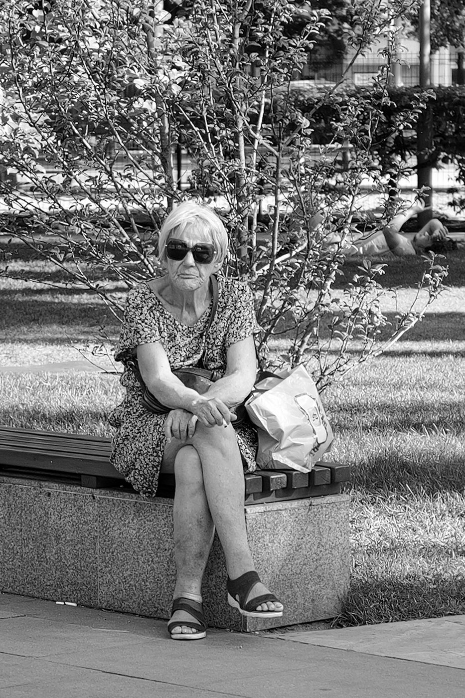 An elderly woman sitting on a bench with a bag and a cigarette, Budapest
