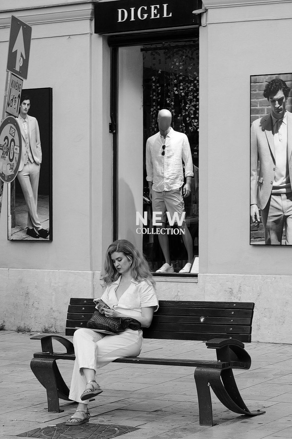 A woman checking her phone on a bench in front of a fashion shop window, Budapest