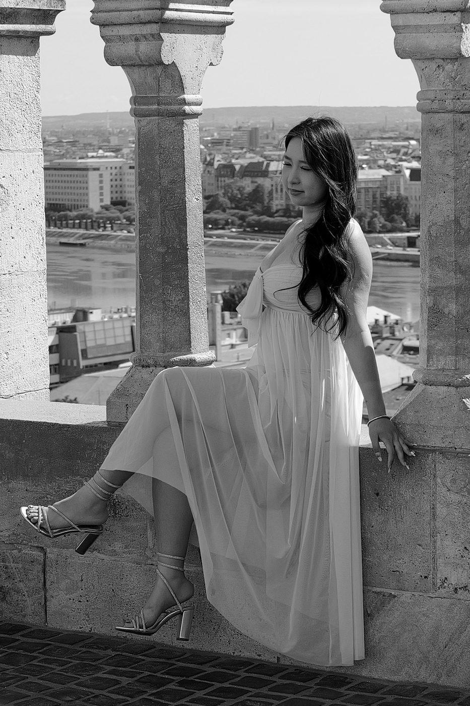 A woman in a flowing dress sitting between two columns of the Bastion, Budapest