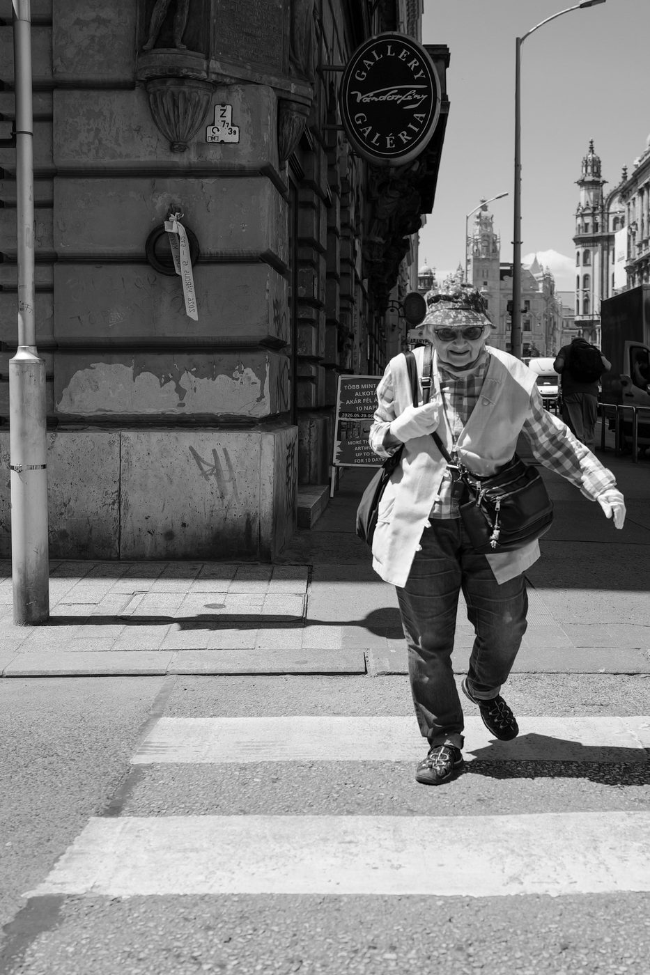 An elderly woman in a straw hat crossing a pedestrian crossing, Budapest