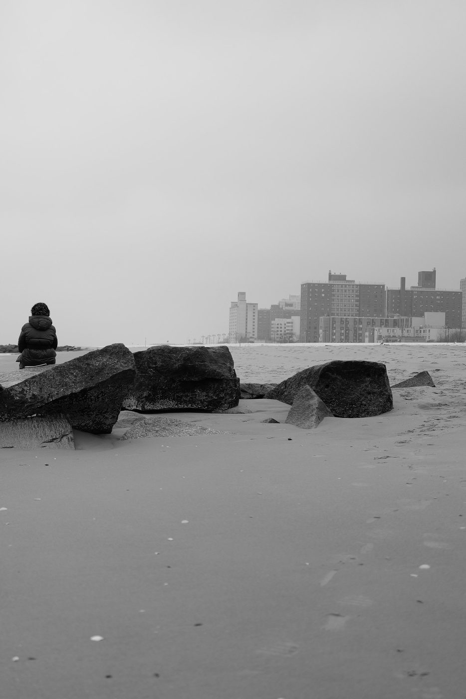 Person sitting on the rocks facing the Coney Island buildings