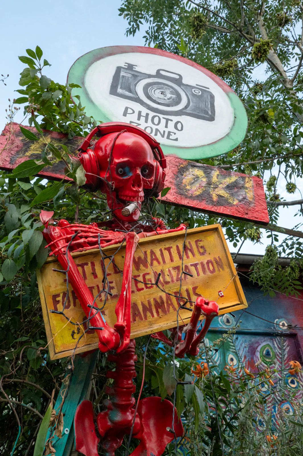 A red skeleton holding a “Still waiting for the legalization of cannabis” sign under a “Photo zone” sign, Christiania, Copenhagen