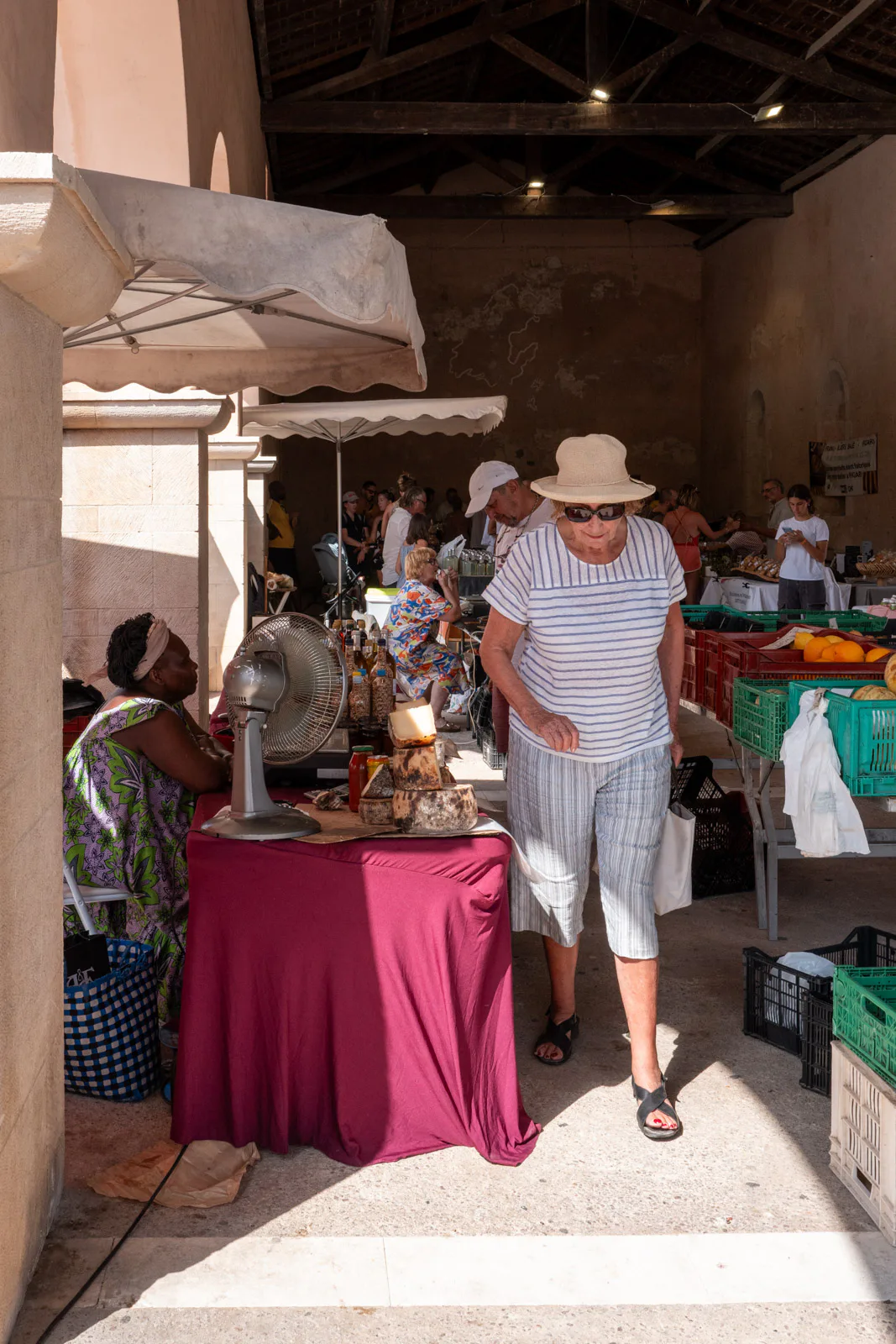 Une dame au chapeau de paille passe devant les étals du marché couvert, Bonifacio, Corse