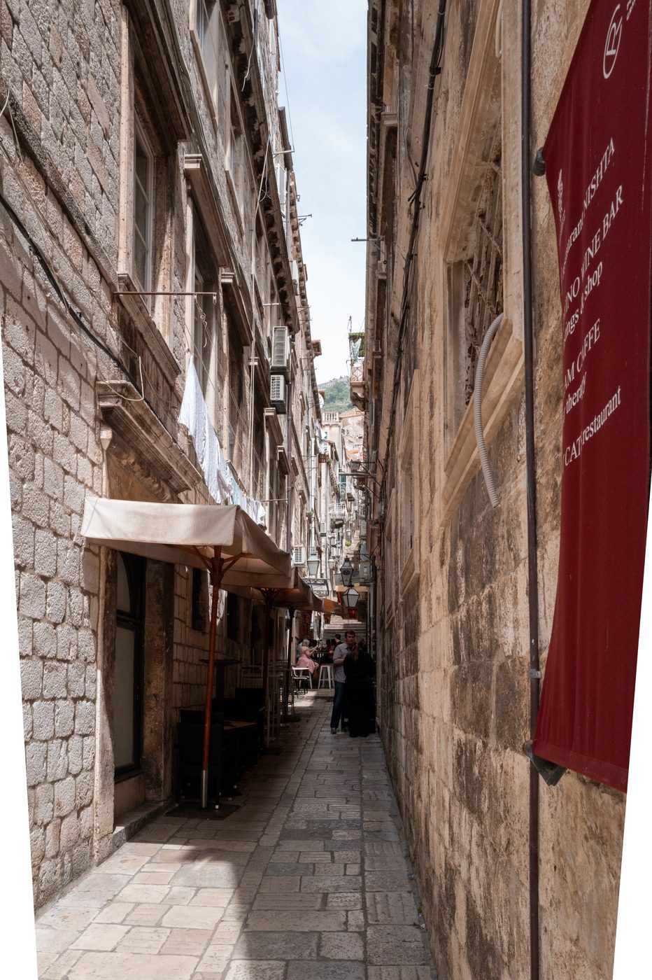 Narrow alley with red signs and a shaded terrace, Dubrovnik