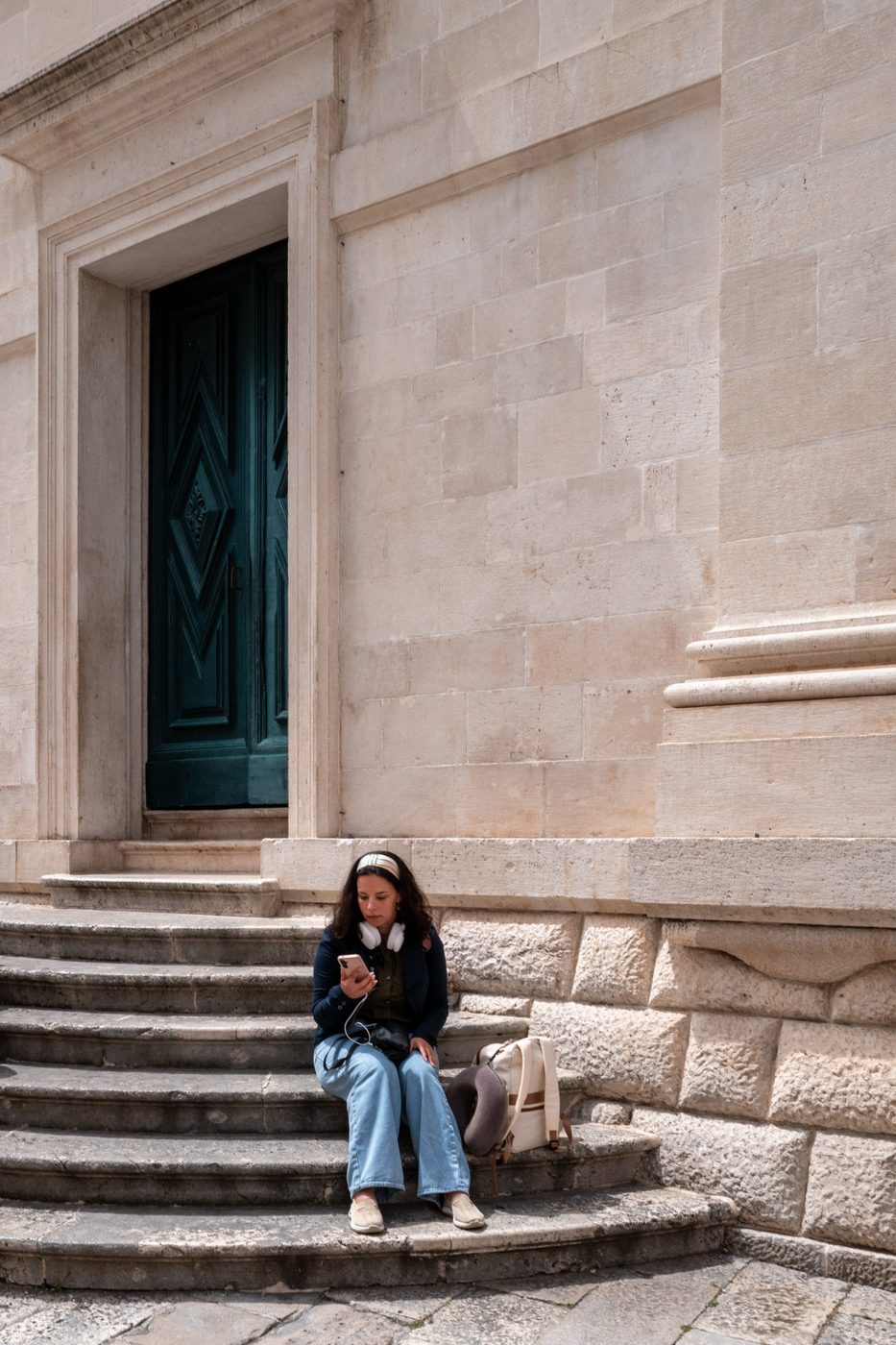 Woman sitting on the steps in front of a green door, absorbed in her phone, Dubrovnik