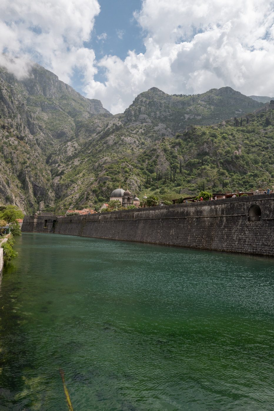 Fortified wall and domes overlooking a green canal surrounded by mountains, Dubrovnik