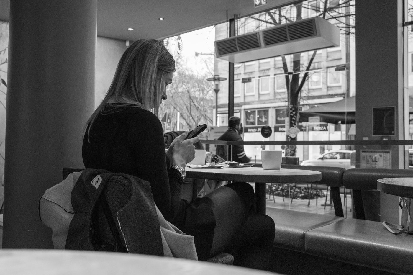 A woman checking her phone at a café table, Düsseldorf