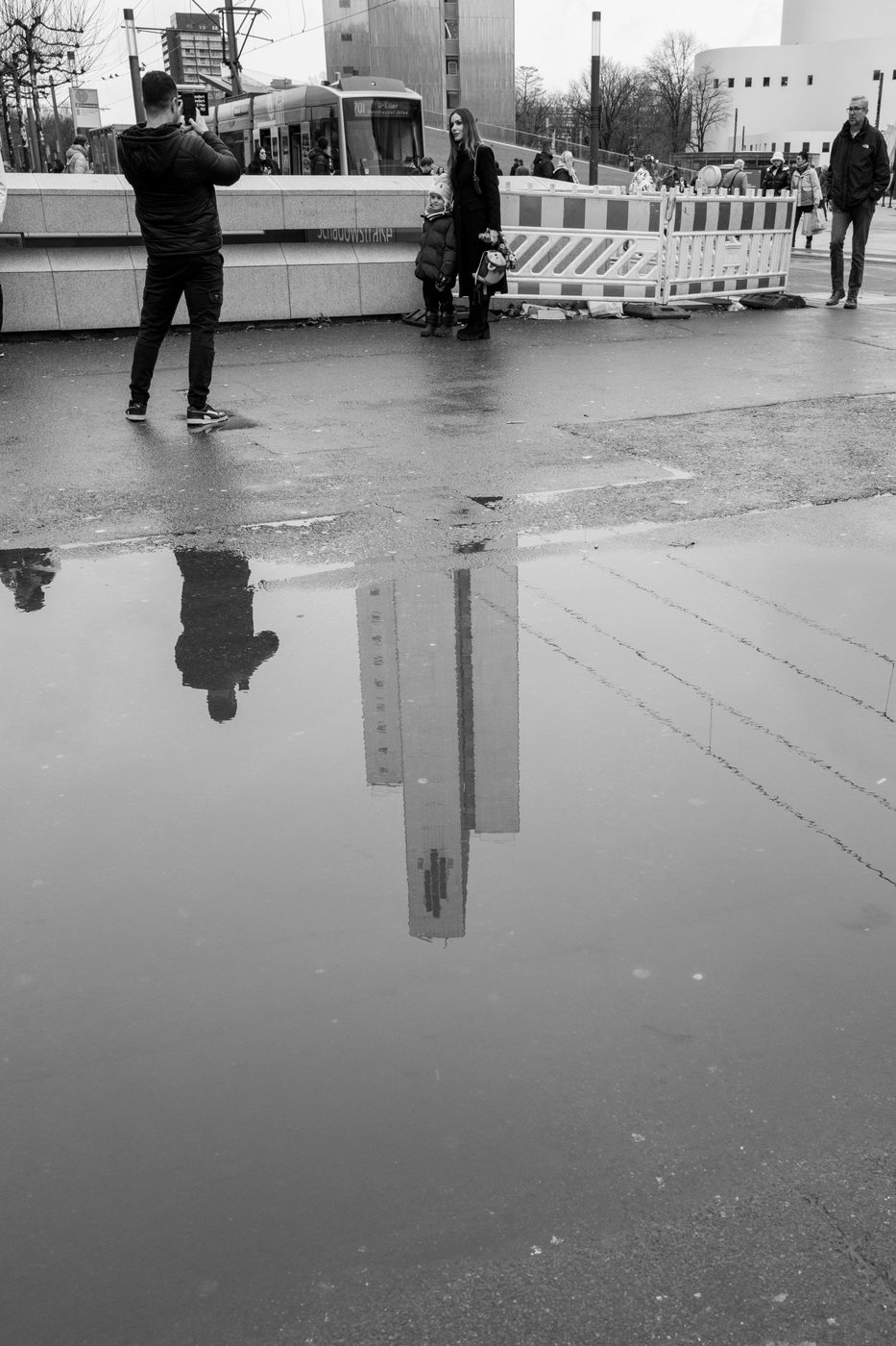 Reflection of a couple and a child in a puddle, wet square, Düsseldorf