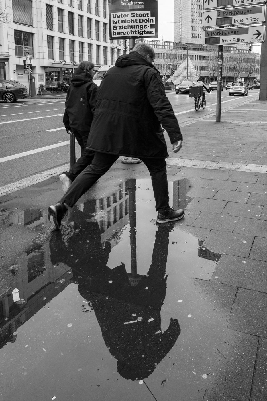 Two people stepping over a puddle in front of an election poster, Düsseldorf