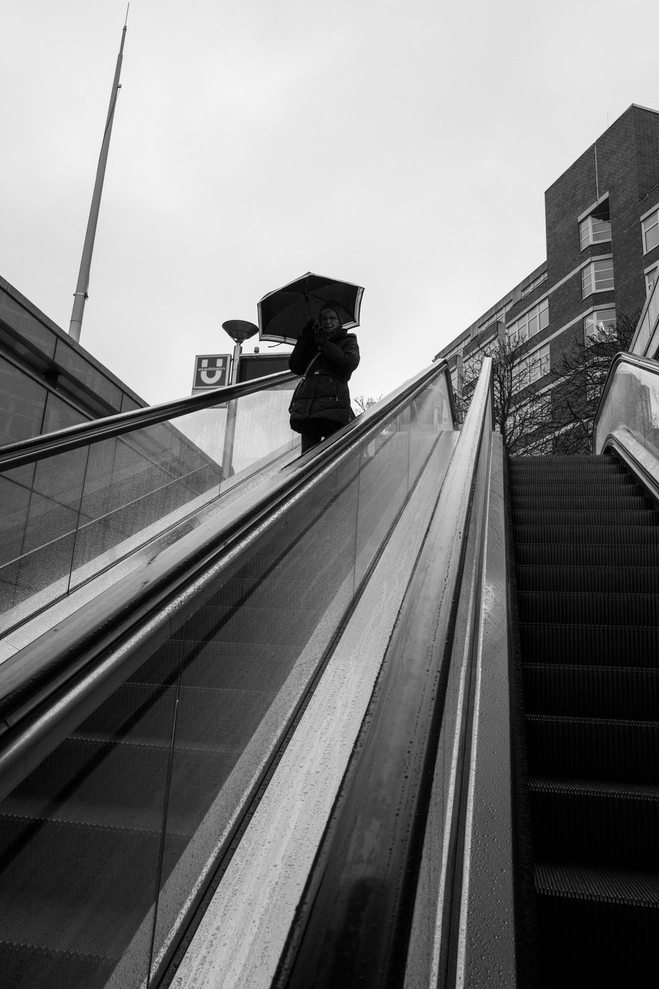 A man under a black umbrella heading down toward an outdoor escalator, Düsseldorf