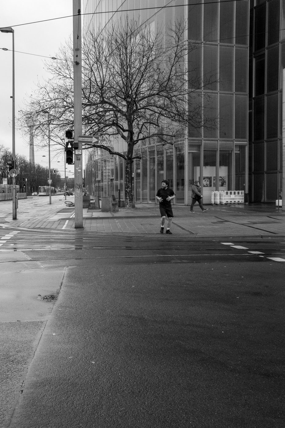 A runner in shorts crossing a deserted intersection in front of a glass facade, Düsseldorf