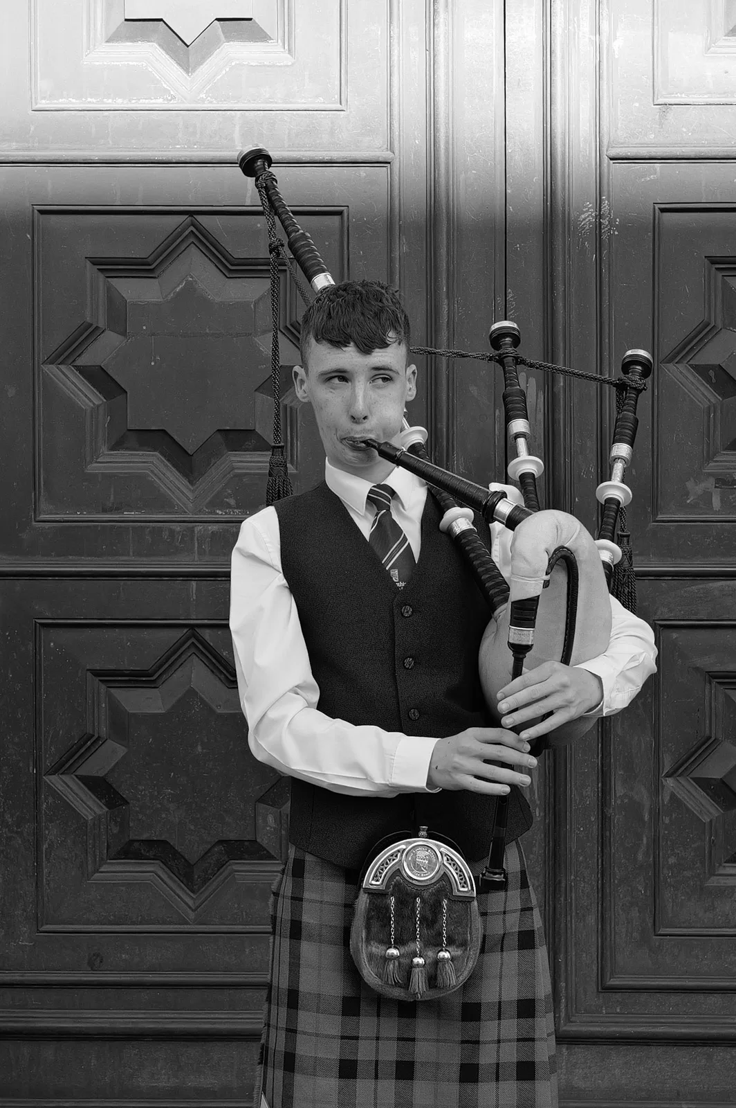 Young piper in a kilt in front of a carved door, Edinburgh
