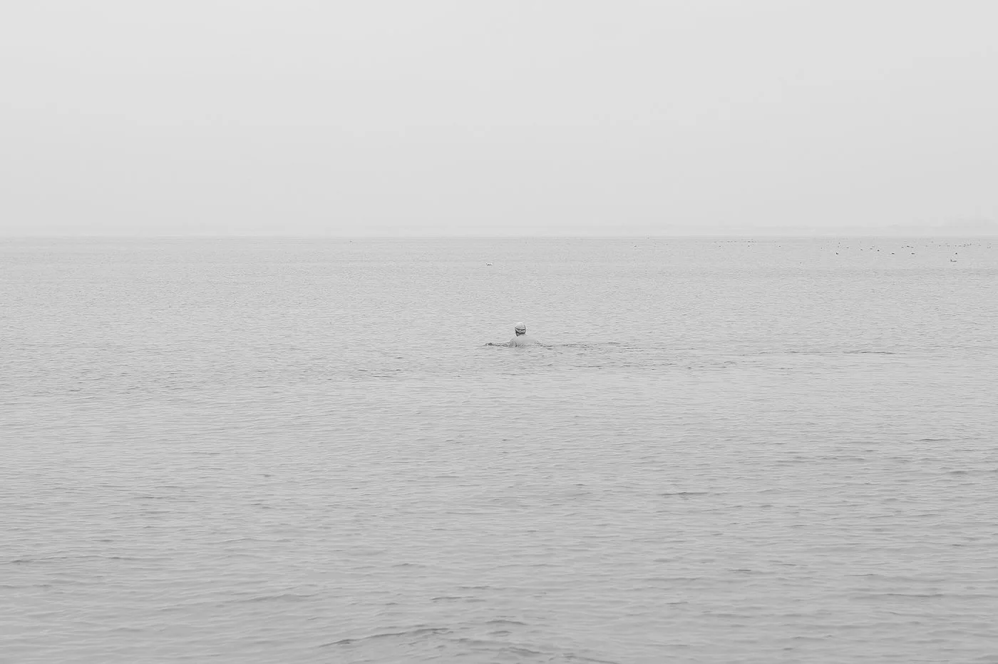 Un nageur au loin dans une mer grise et calme, Coney Island, New York