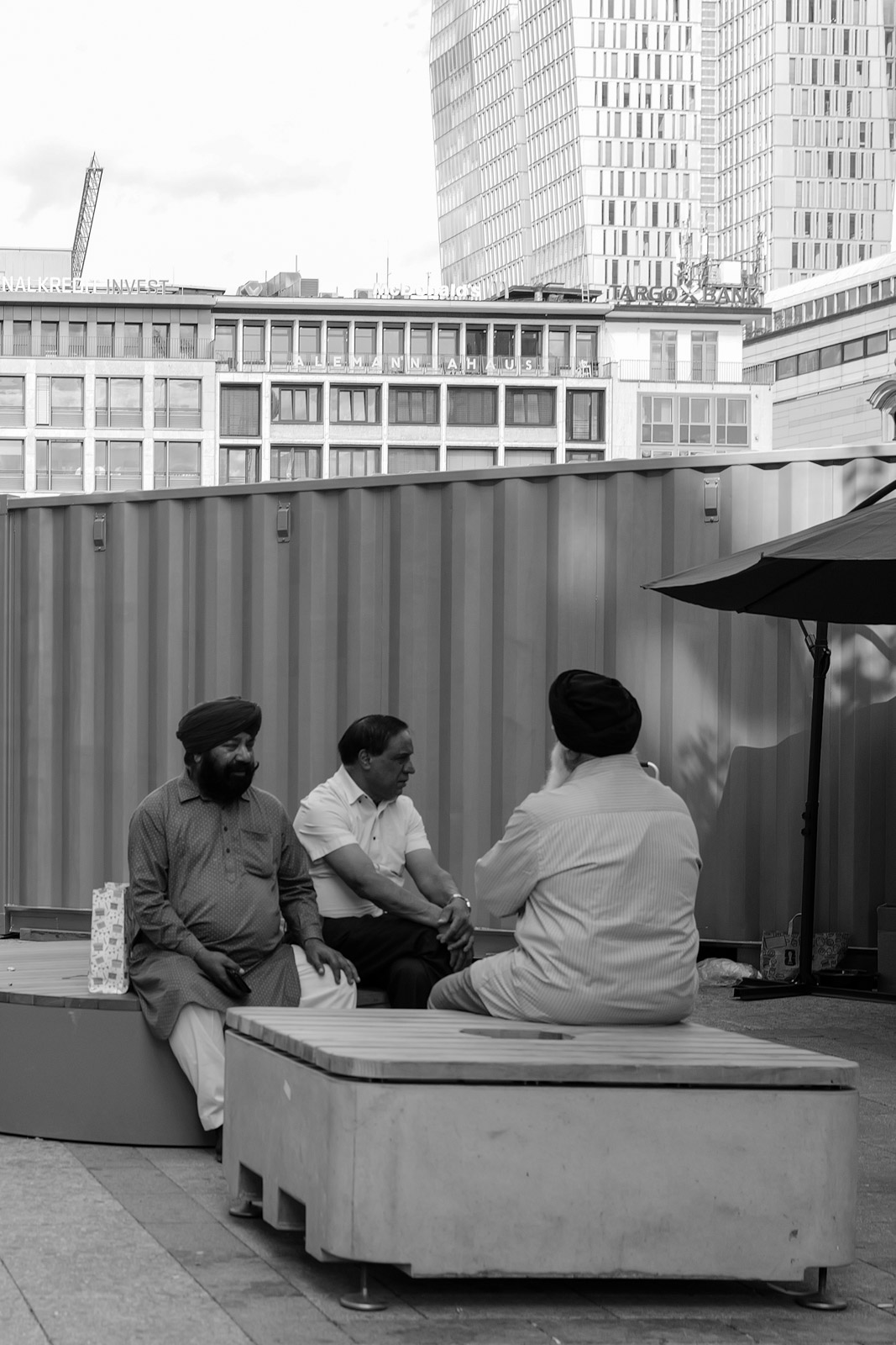 Trois hommes assis sur un banc de pierre devant un batiment moderne, Francfort