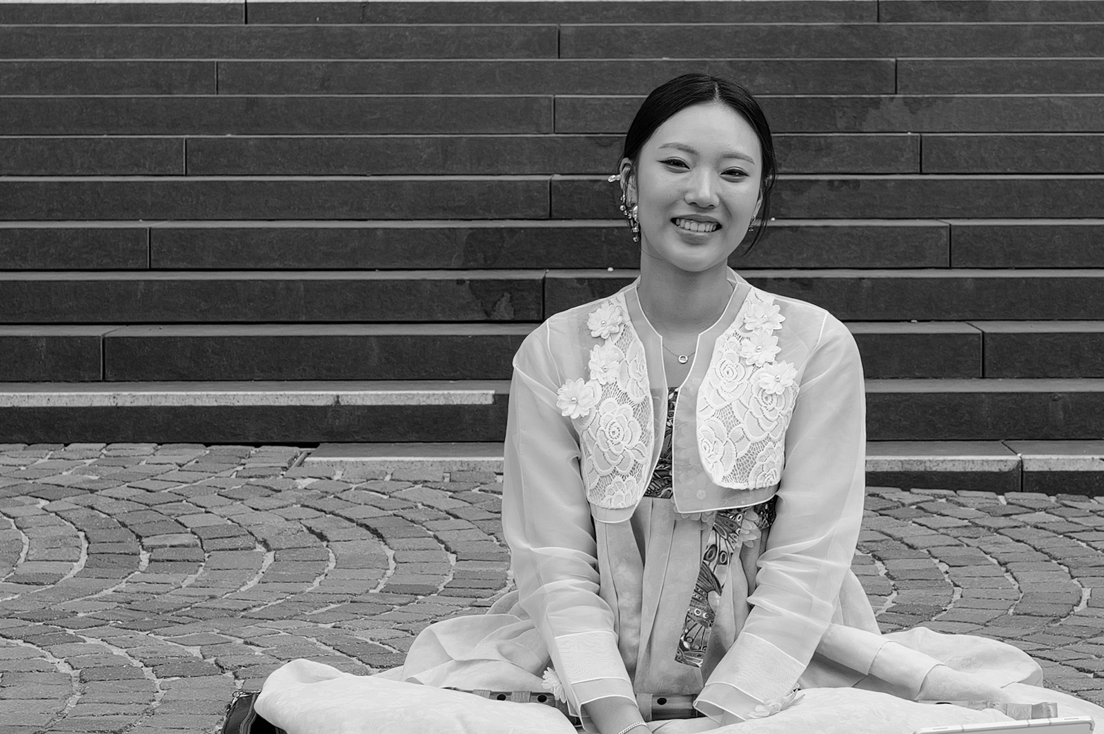 Jeune femme assise en tailleur sur des marches en pierre, souriante, Francfort