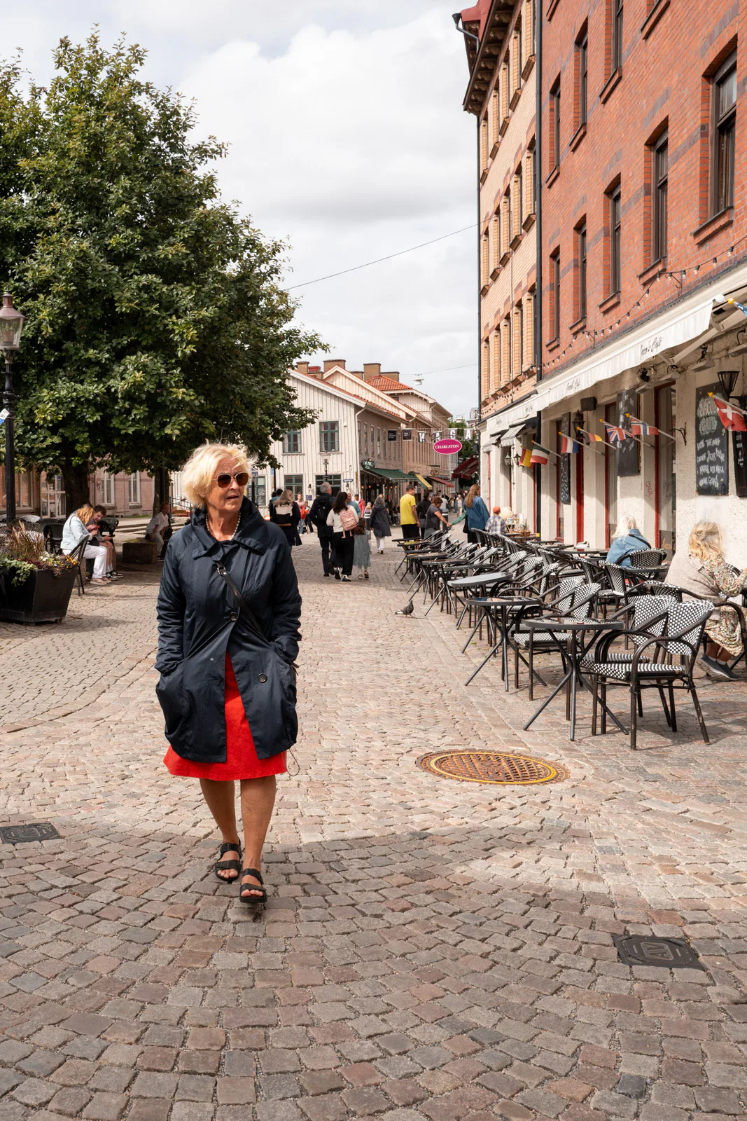 A woman in a red skirt walking up a cobbled street lined with terraces, Haga, Gothenburg