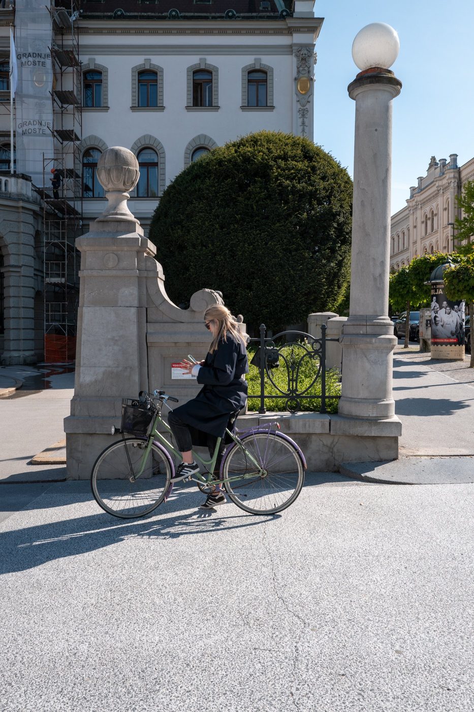 Cyclist checking his phone near a stone gateway, Ljubljana