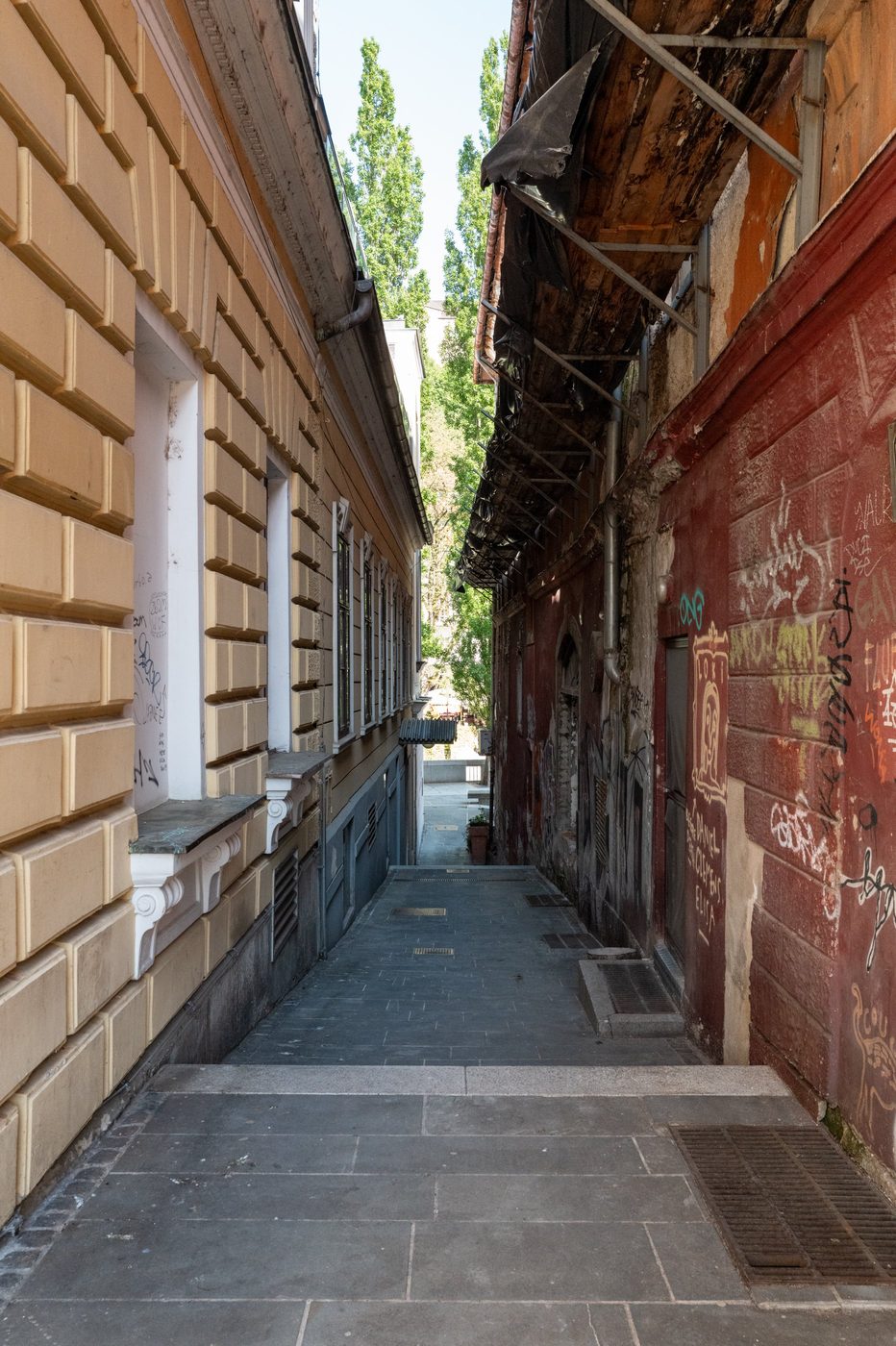 Narrow alley between a beige facade and a red graffiti-covered wall, Ljubljana