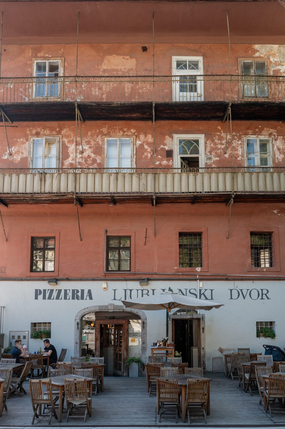 Terrace of the Pizzeria Ljubljanski Dvor beneath a faded pink facade, Ljubljana