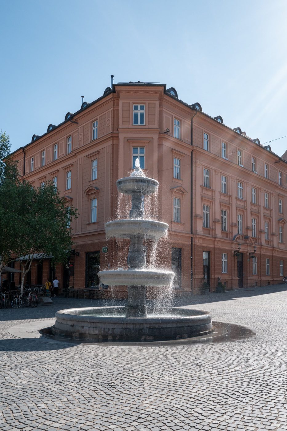 Tiered fountain gushing in front of a pink building, Ljubljana