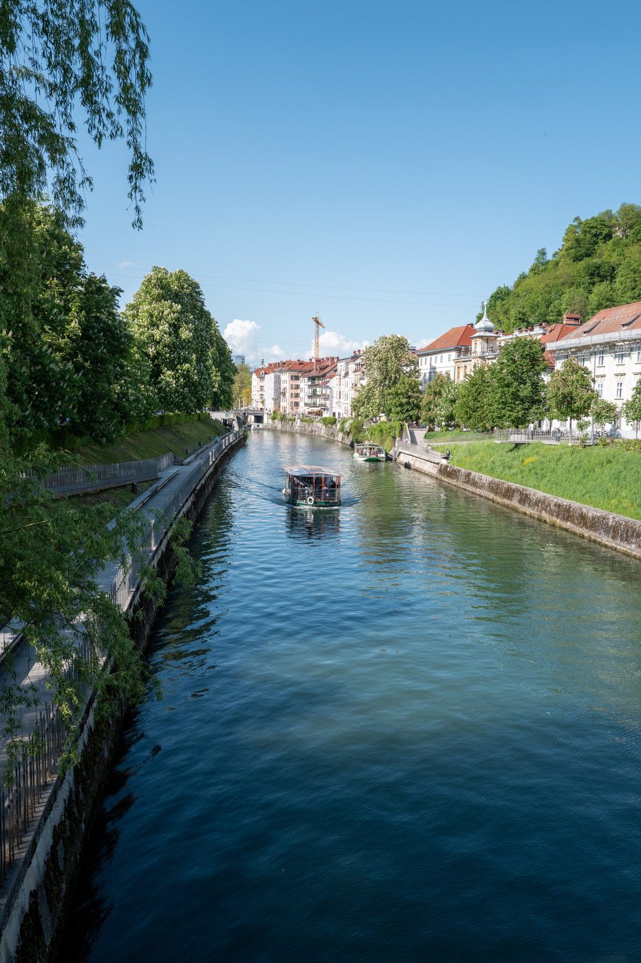 Tour boat gliding along the river toward the wooded hill, Ljubljana