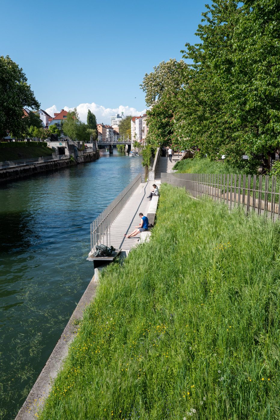 Walkers sitting on the steps by the lush green water, Ljubljana