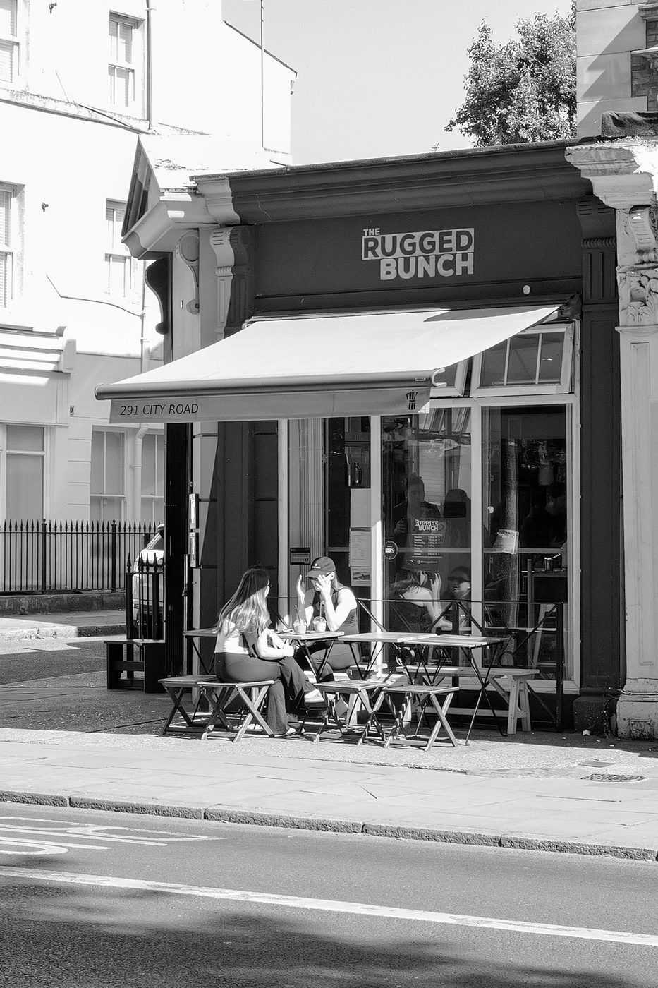 Two customers seated on a terrace under the awning of a neighbourhood cafe, London