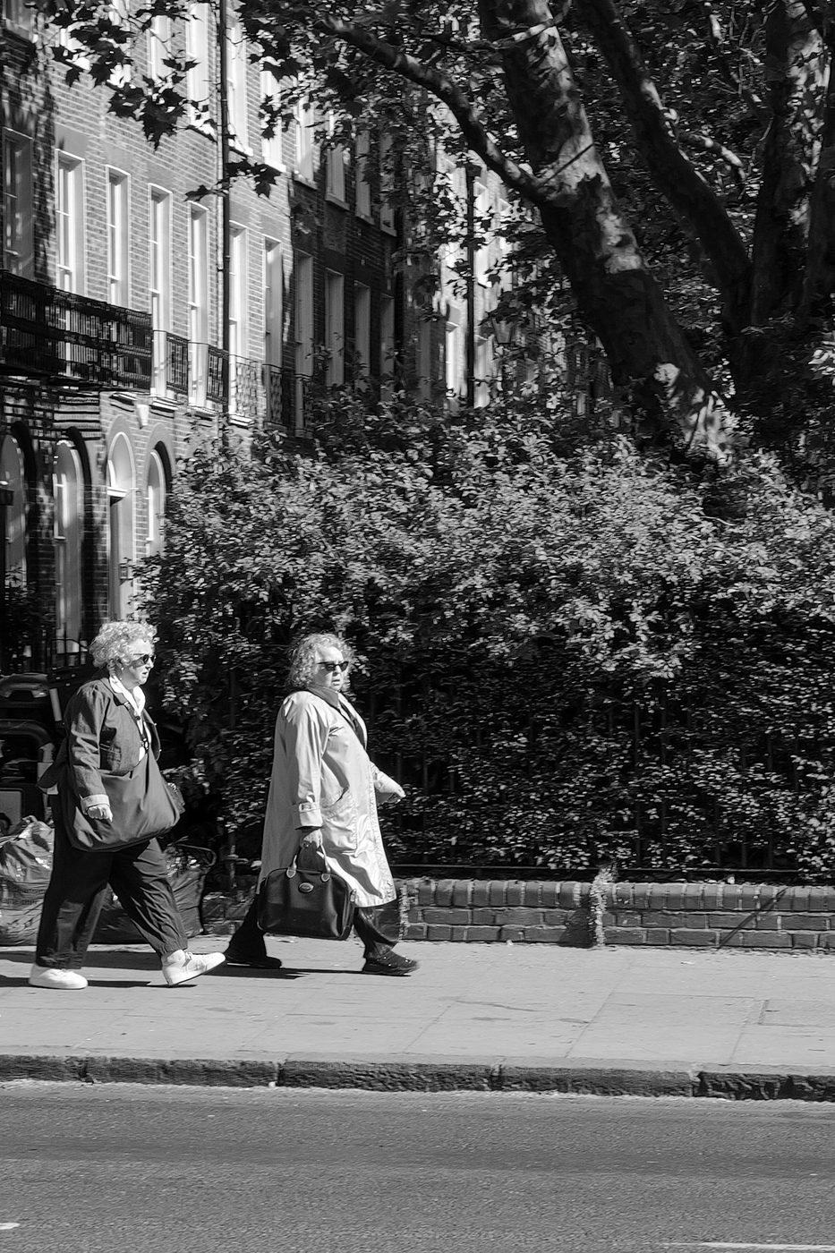 Two passers-by walking along a sun-drenched brick facade, London