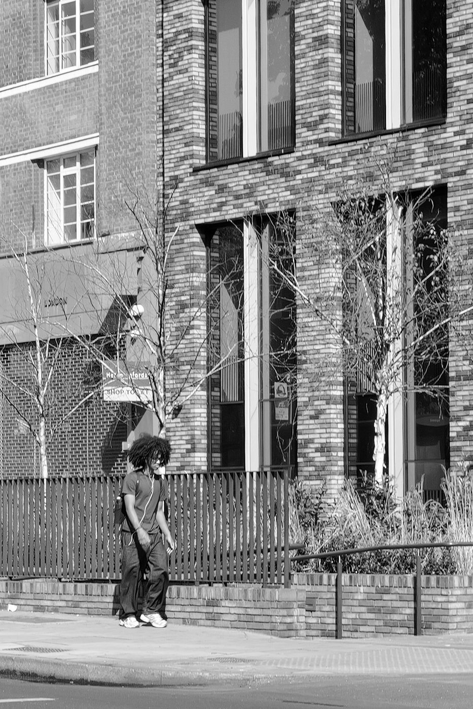 Young man standing still near bare trees in front of a brick building, London