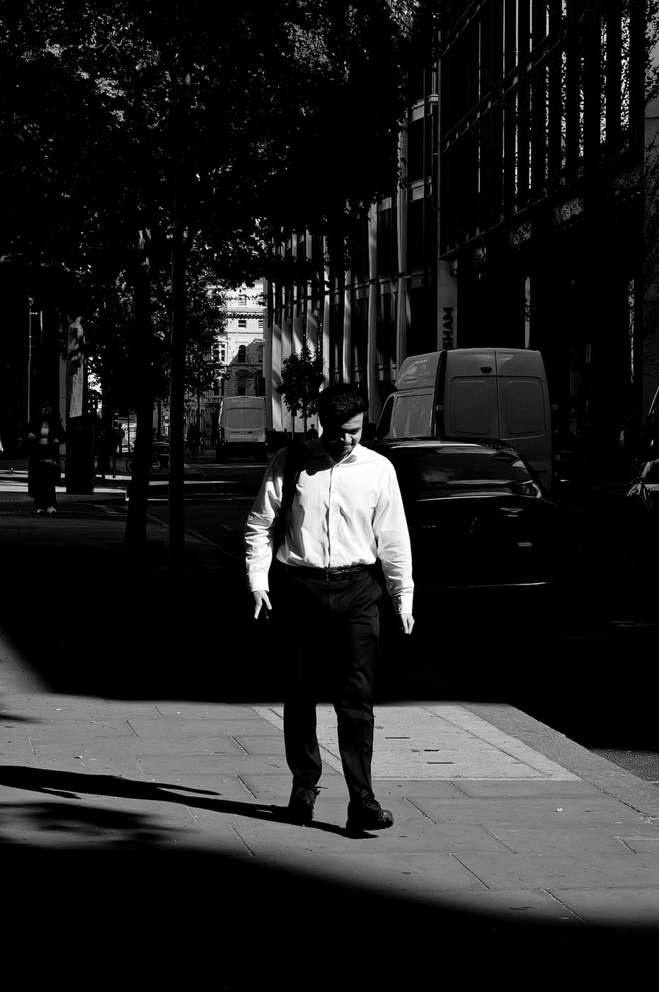 Silhouette of a pedestrian crossing a strip of harsh light between shadow and sun, London