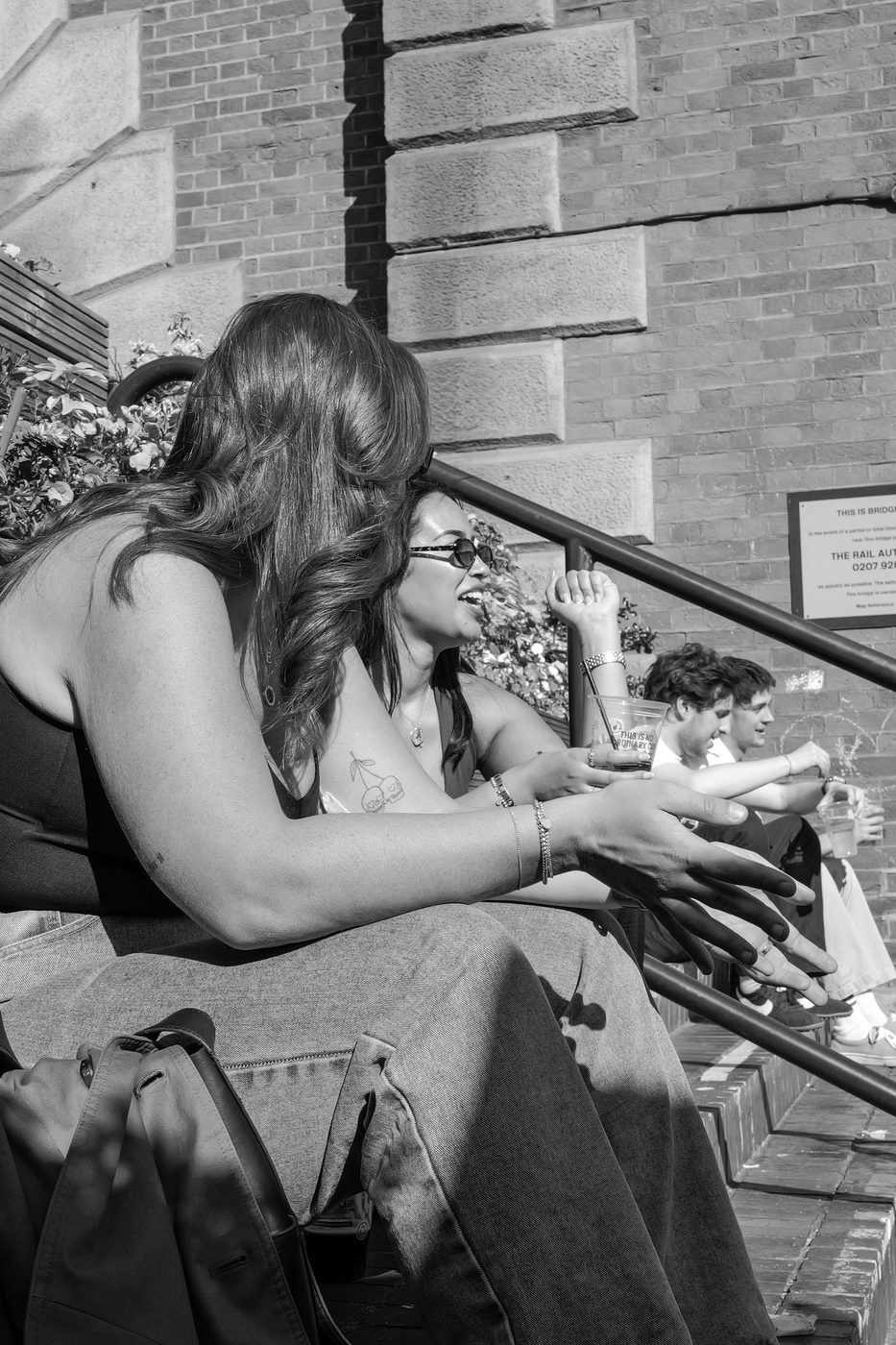 Two friends laughing on some steps, drinks in hand in the sun, London