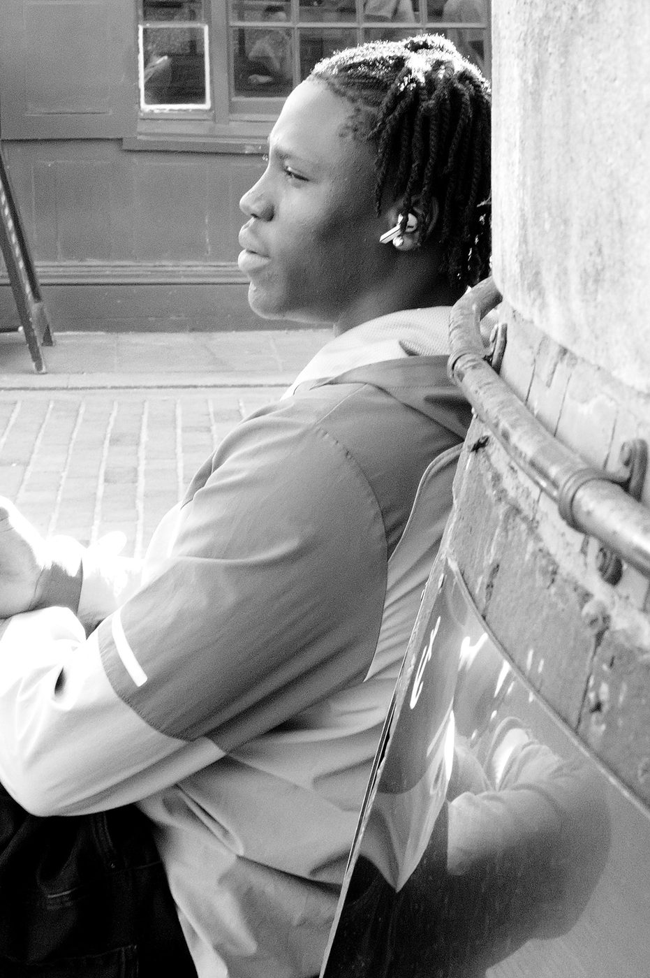 Young man leaning against a wall, wireless earbud in, gazing at the street, London
