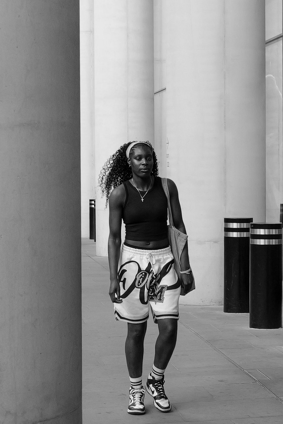 Young woman in basketball shorts crossing a colonnaded passage, London