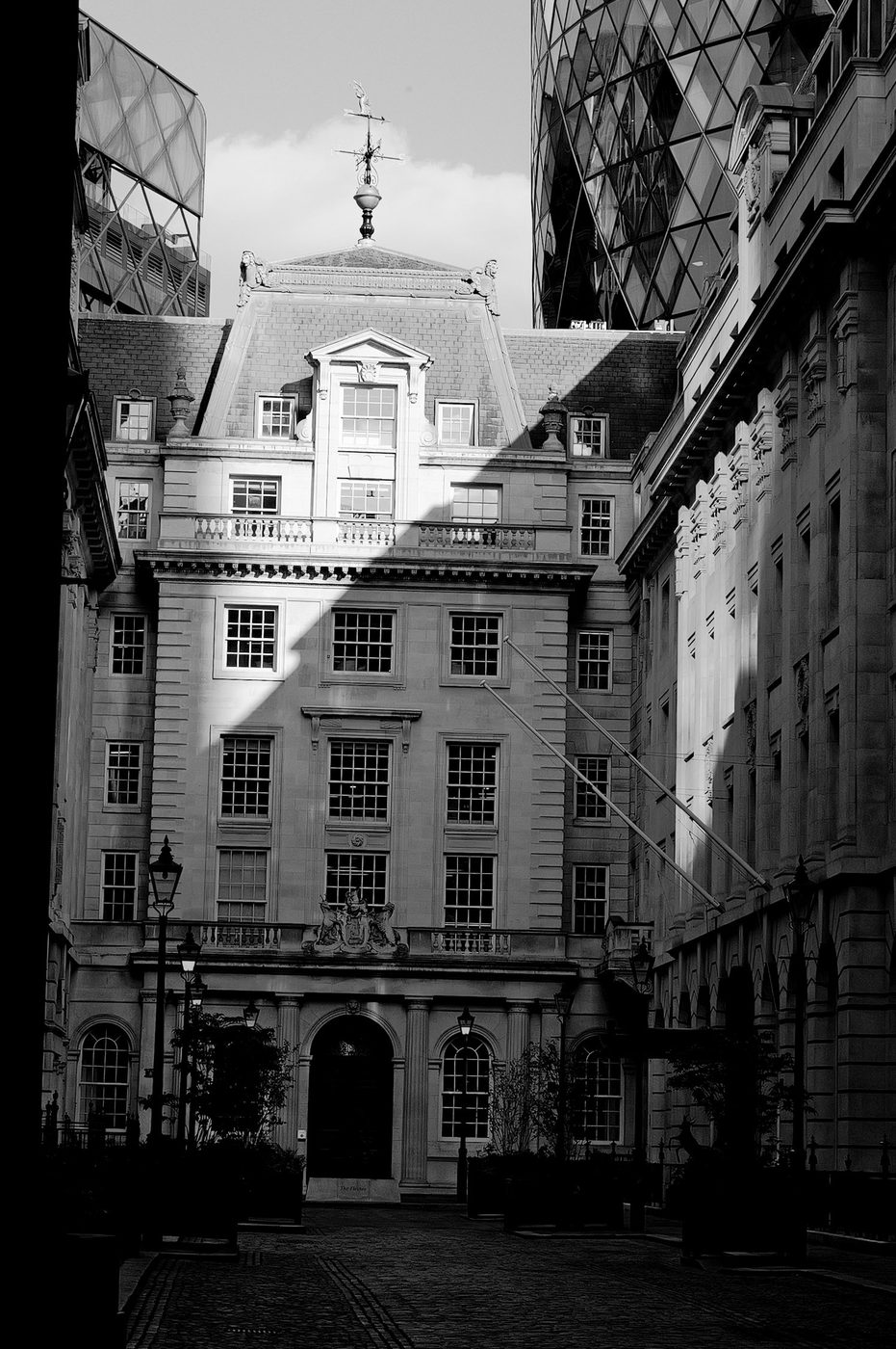 Period building topped with a weathervane, framed by modern towers including the Gherkin, London