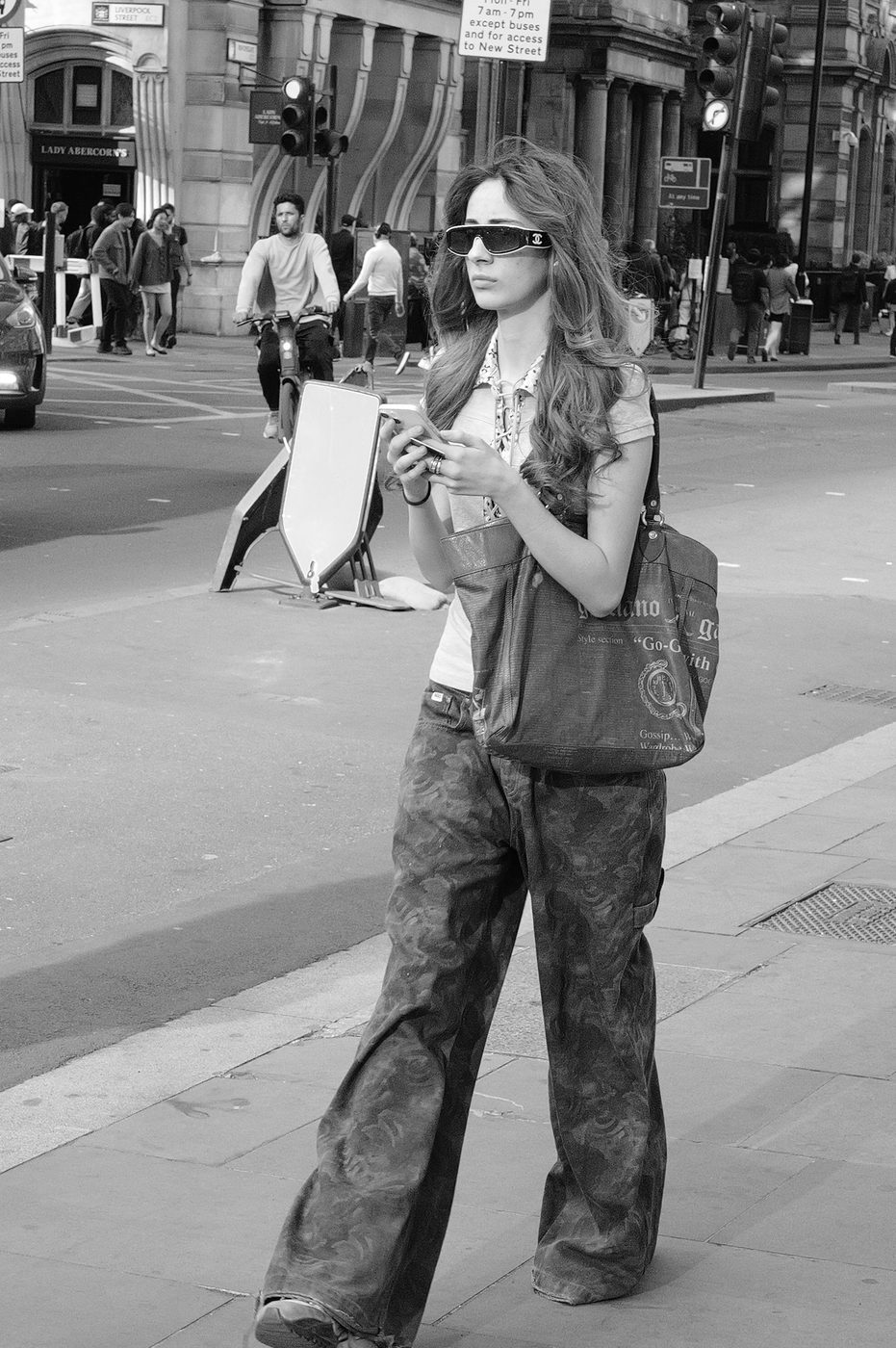 Young woman in sunglasses crossing the street while checking her phone, London