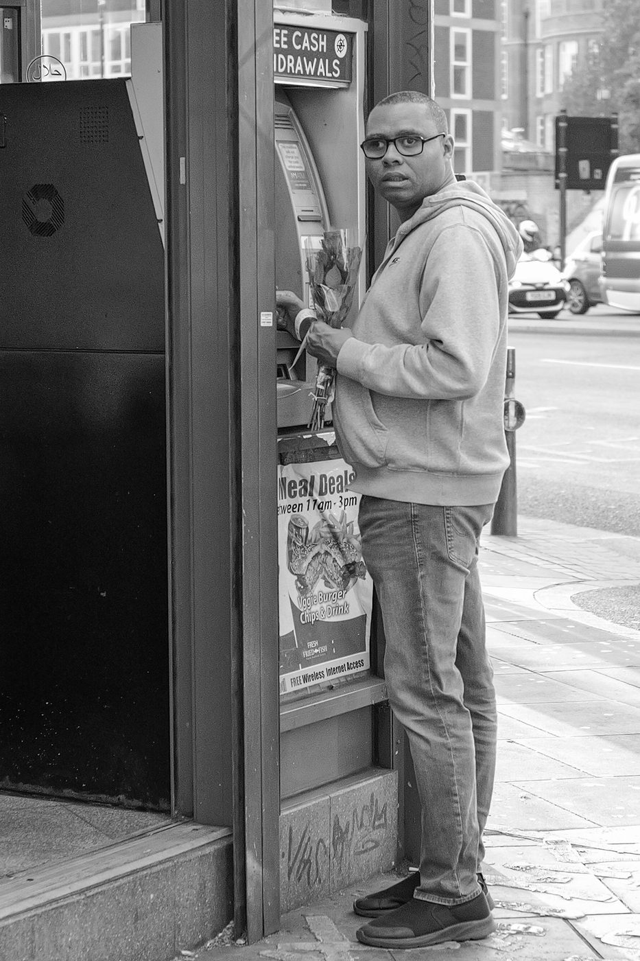 A man withdraws cash from an ATM, bouquet of flowers in hand, London