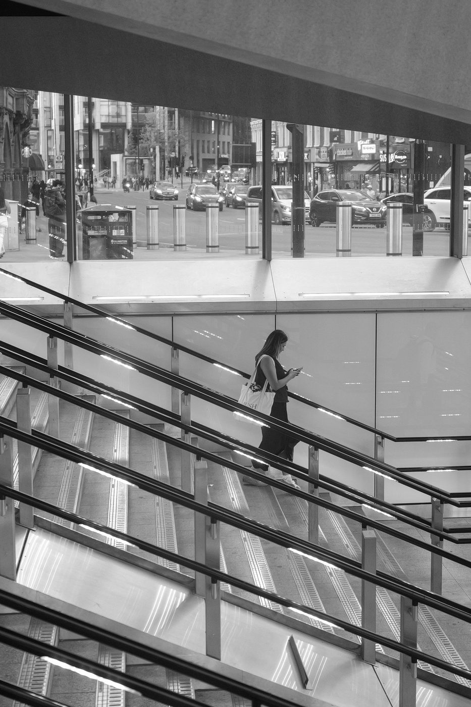 Silhouette of a woman going down a glass staircase, phone in hand, London