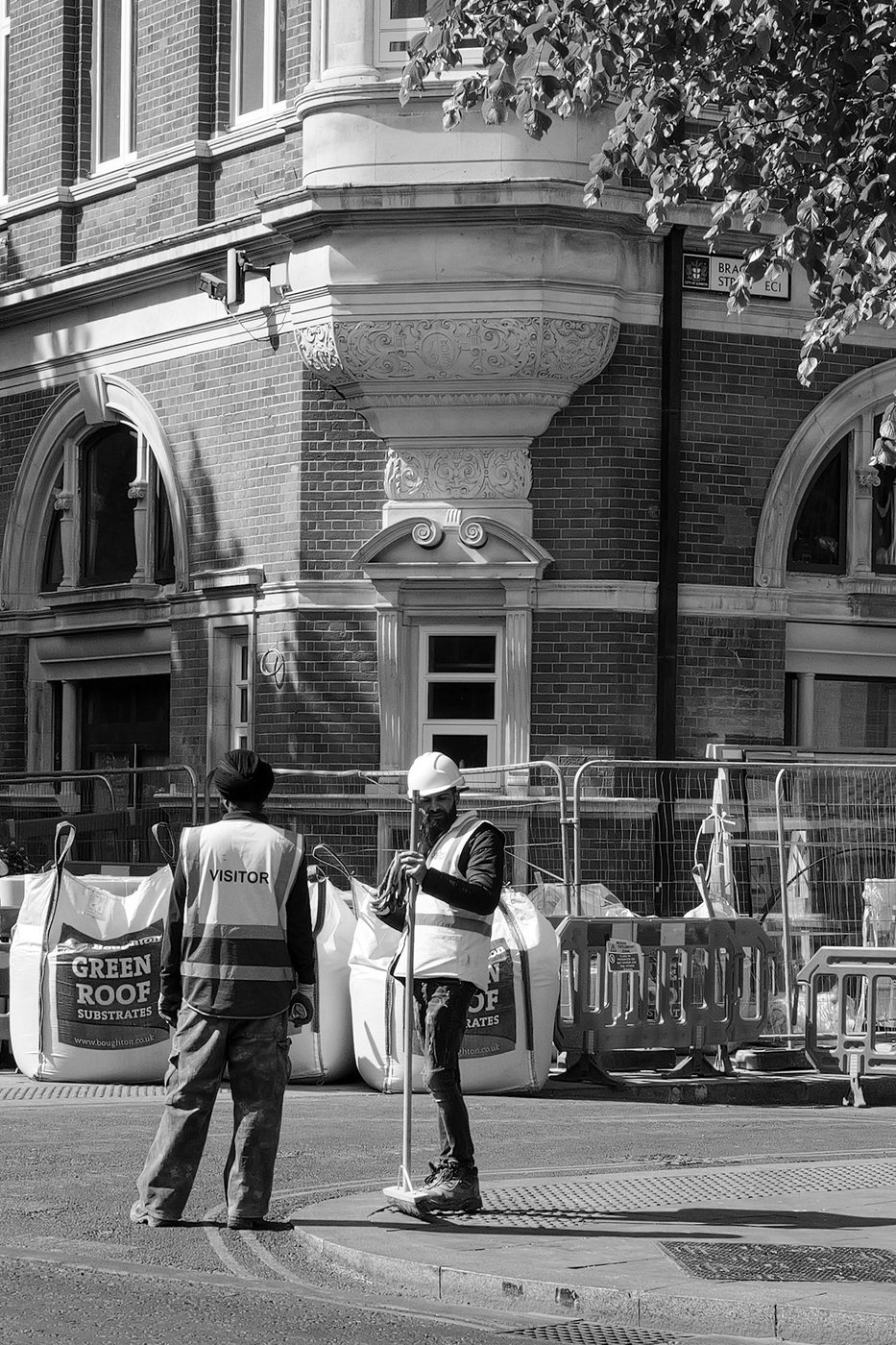 Two construction workers talking in front of a brick facade decorated with sculptures, London