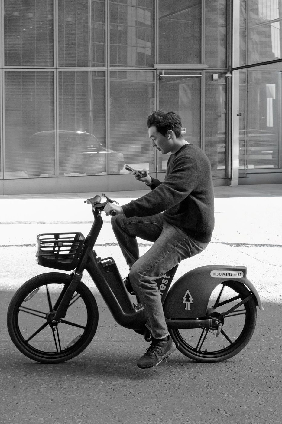 Cyclist checking his phone while pedalling a bike-share bicycle, London