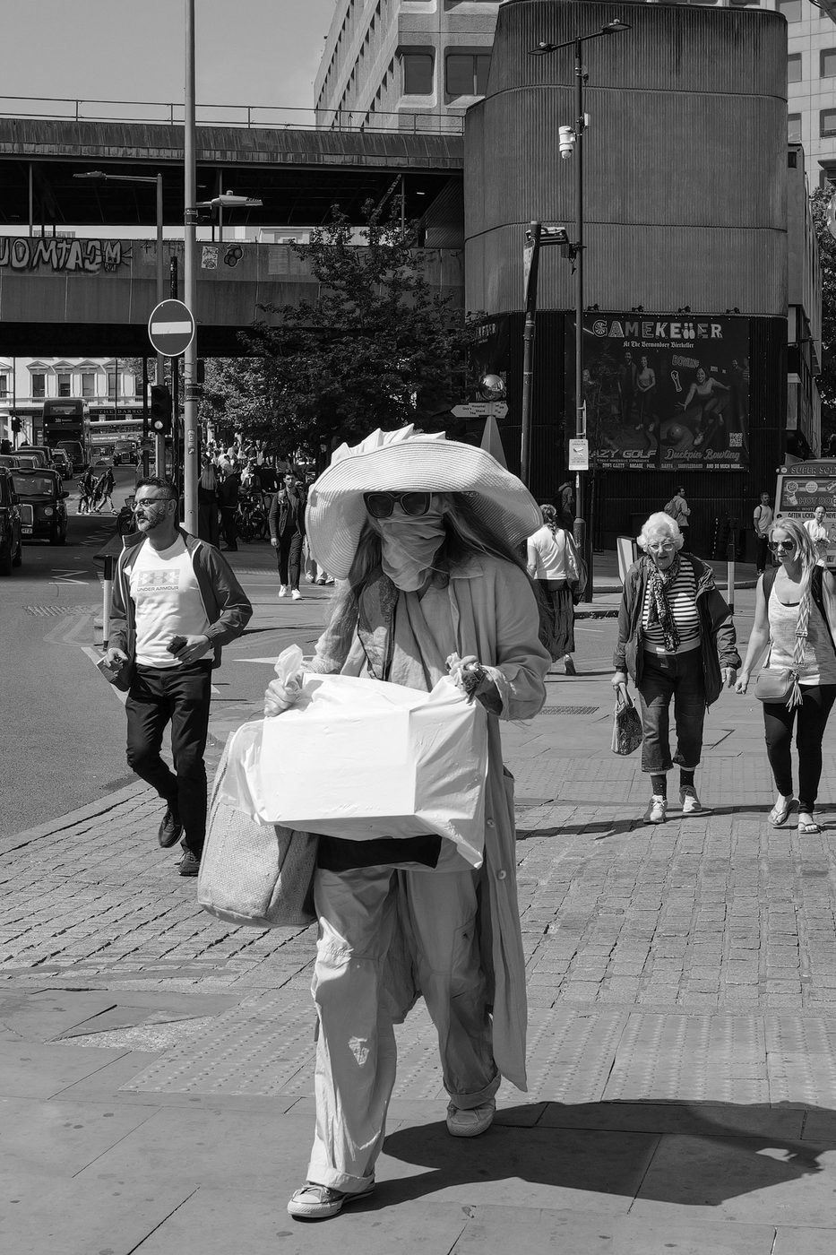 Enigmatic silhouette of a woman in a wide-brimmed hat and mask, paper bag in hand, London